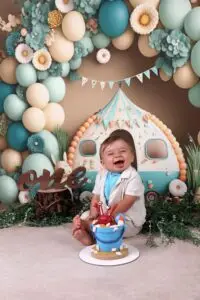 Μωρό αγόρι χαμογελά μπροστά σε τούρτα με θέμα παραλία, σε διακοσμημένο σκηνικό για φωτογράφιση cake smash πρώτων γενεθλίων