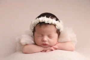 Νεογέννητο μωρό σε πόζα με στήριξη, με λευκή κορδέλα στο κεφάλι, φωτογραφημένο στο Alexia Newborn Photography.